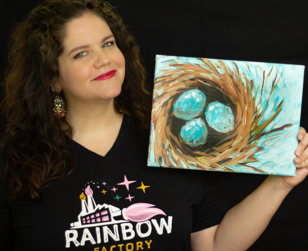 A woman holding up a painting of a bird's nest at a party venue.