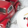 A red toy truck with paint and paintbrushes on a white plate.
