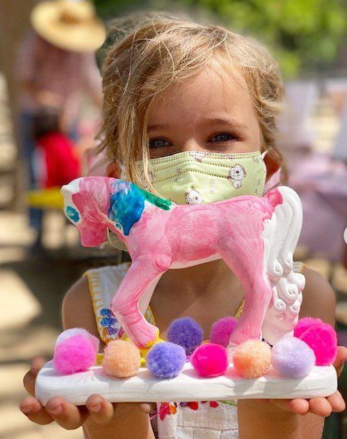 A little girl holding a pink horse with pom poms.