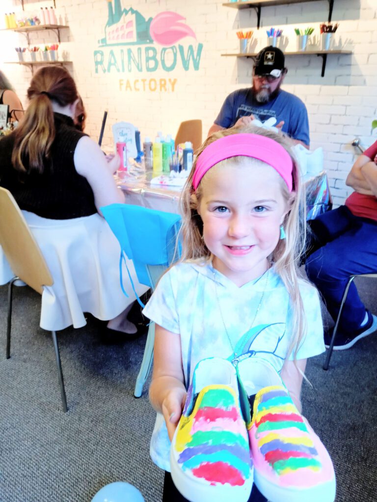 A little girl holding up a pair of colorful shoes.