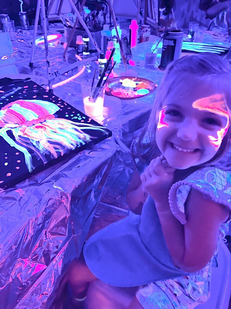 A little girl sitting at a table with glow in the dark paint at a party venue.
