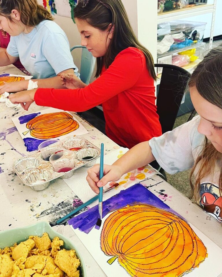 A group of girls painting pumpkins at a table.