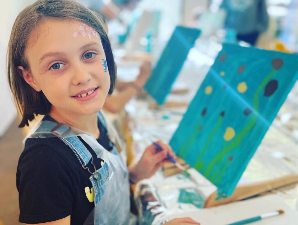 A girl smiles while painting at an art studio.