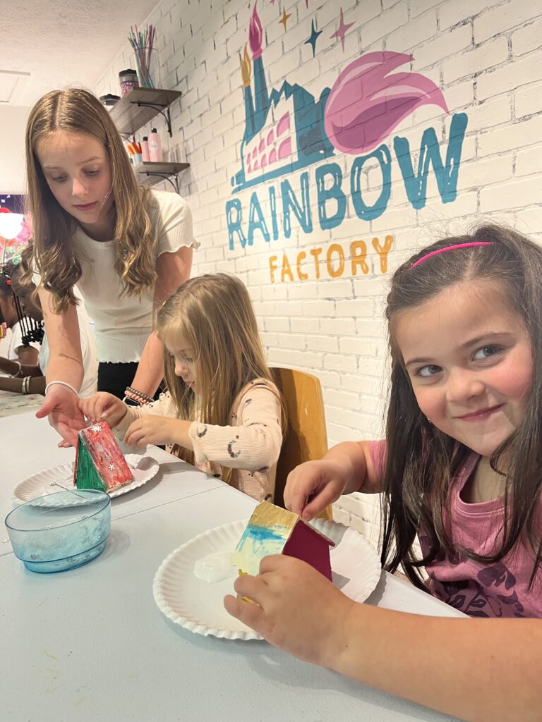 A group of girls at a table making crafts at the rainbow factory.