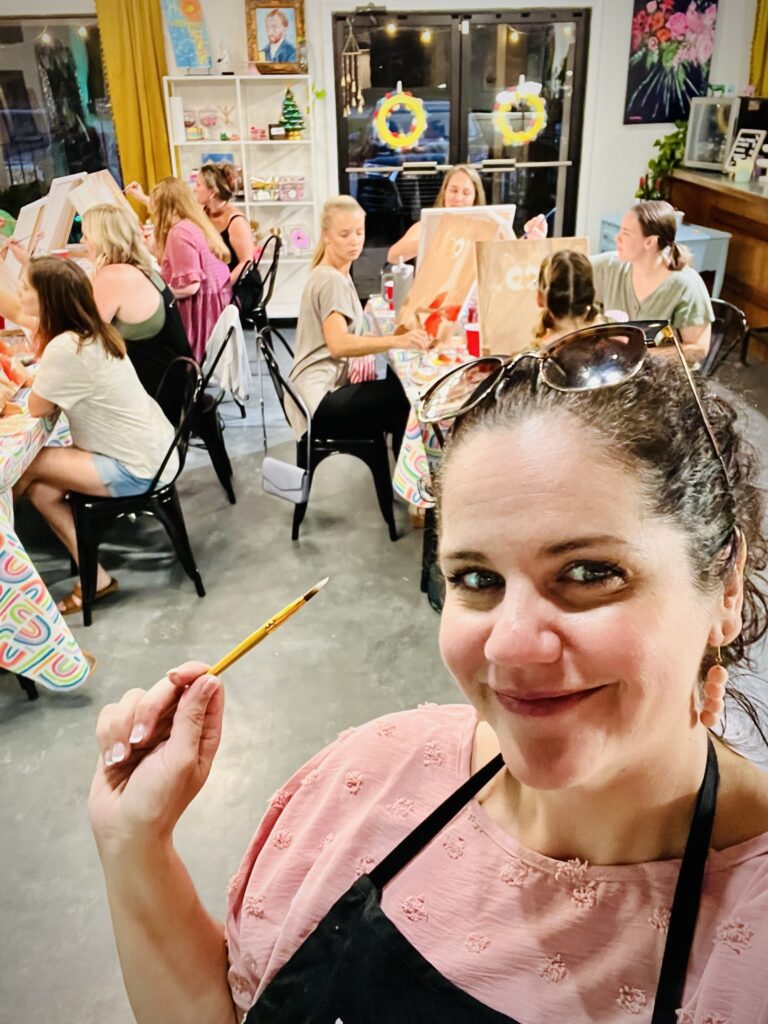 A woman holding a paint brush in front of a group of people.