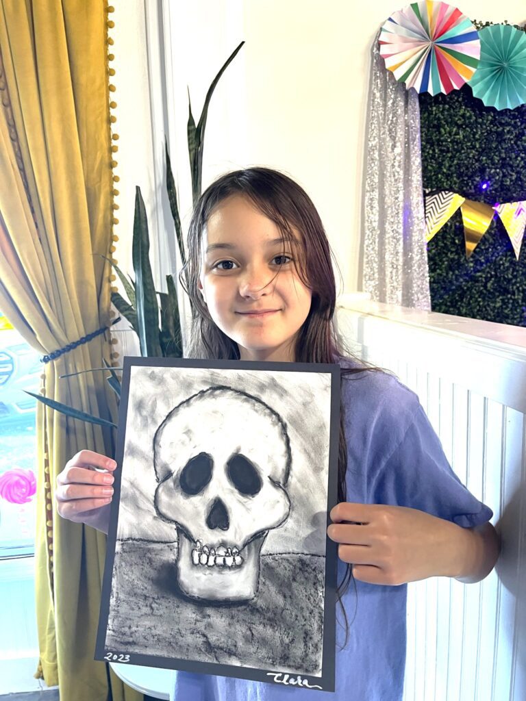 A girl holding up a drawing of a skull.