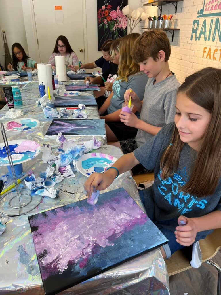A group of young people painting at a table.