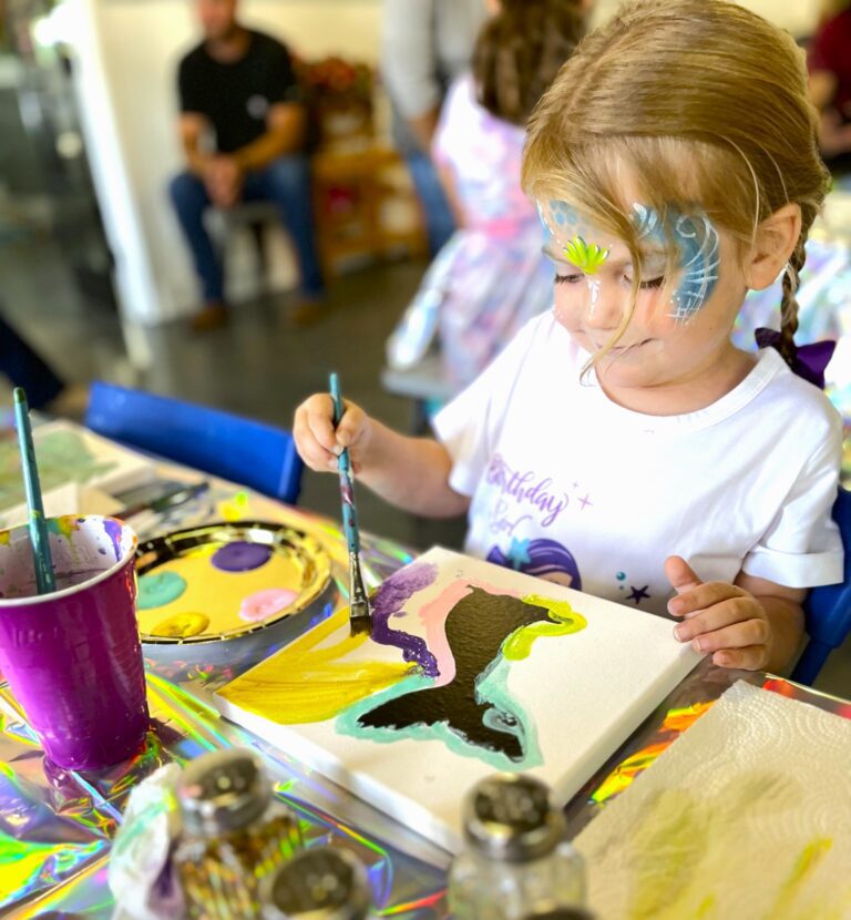 A little girl with face paint on her face painting.