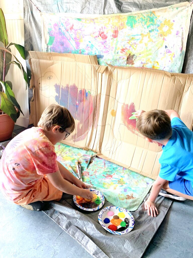 Two young boys painting with paint on a canvas.