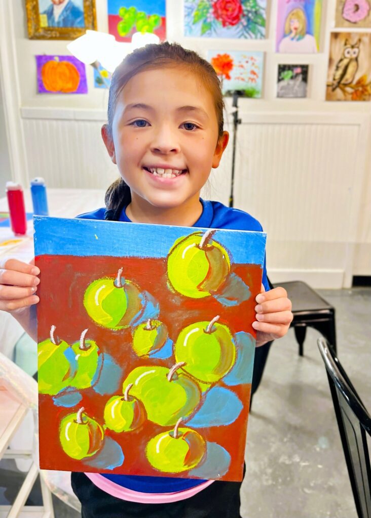 a girl is holding up a painting of apples