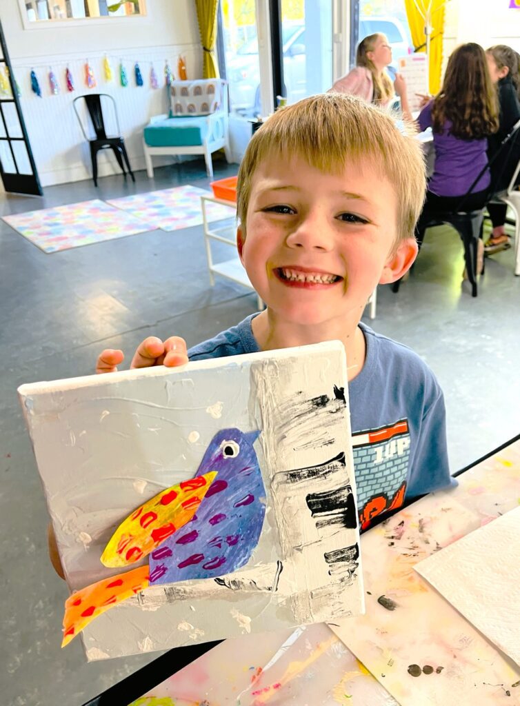 a boy is holding up a painting of a bird