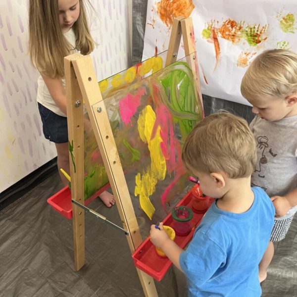 Three children playing with paint on an easel.