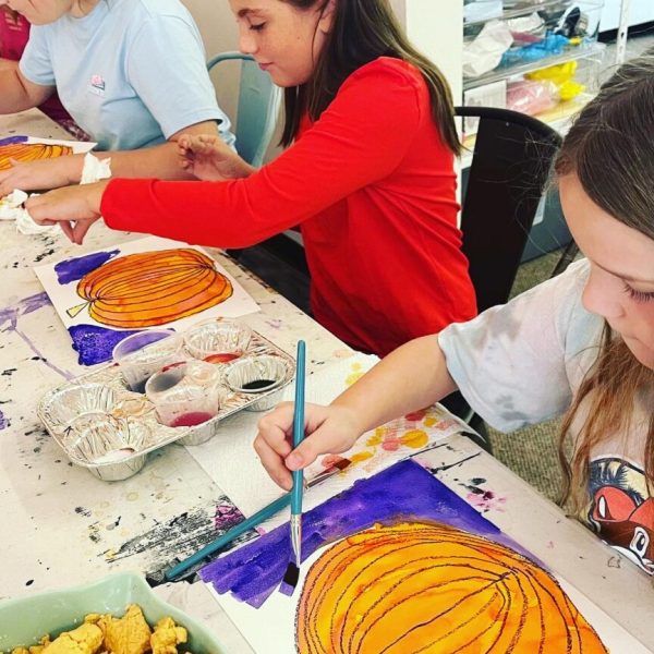 A group of girls painting pumpkins at a table.