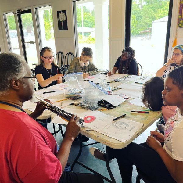A group of people sitting around a table with paper and pencils.