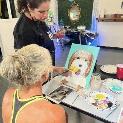 Two women painting a picture of a dog.