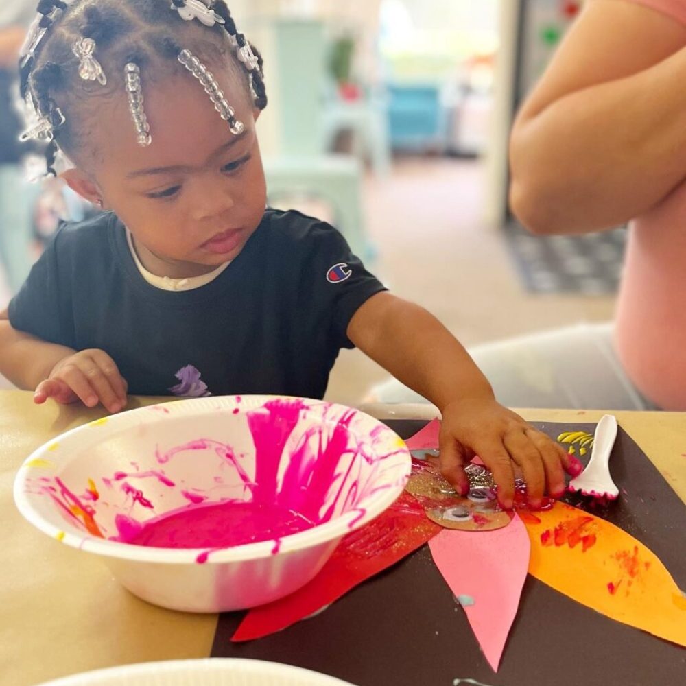 A young girl is playing with paint at a table.