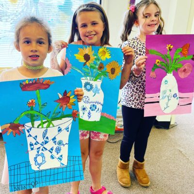 A group of girls holding up flower paintings.