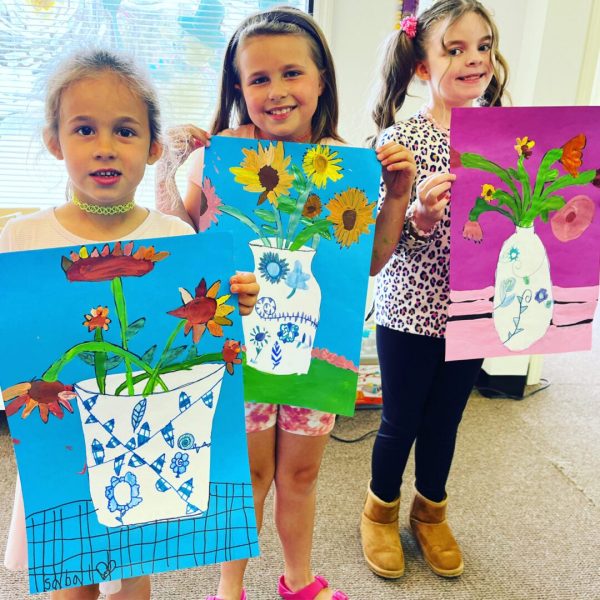 A group of girls holding up flower paintings.