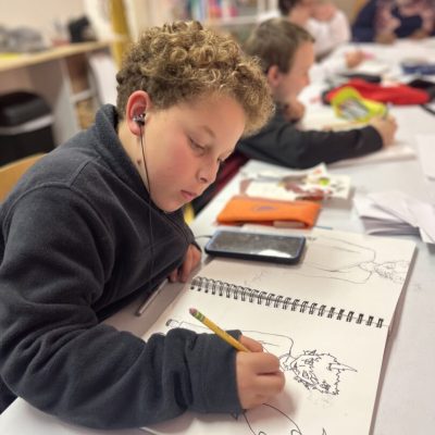 A boy is drawing at a table in a classroom.