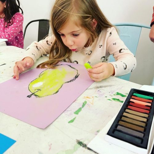 A little girl is painting with crayons at a table.