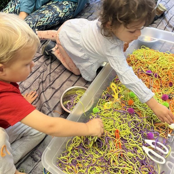 A group of children playing with colorful string in a plastic container.
