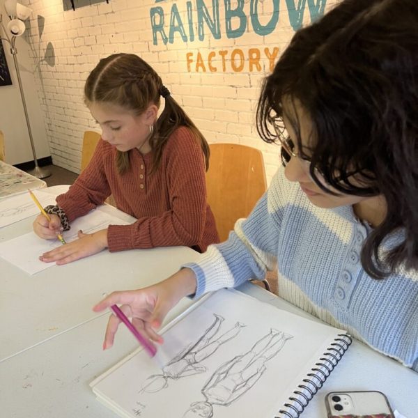 Two girls drawing at a table in a rainbow factory.