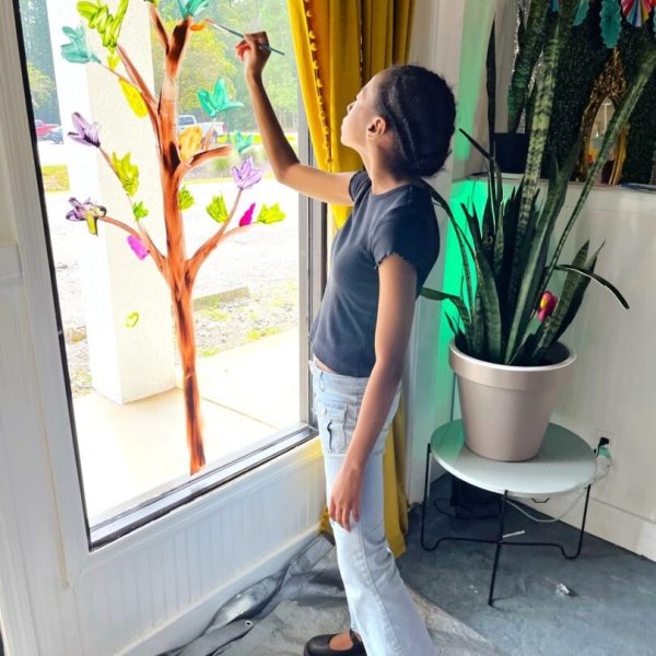 A woman is painting on the window of her house.