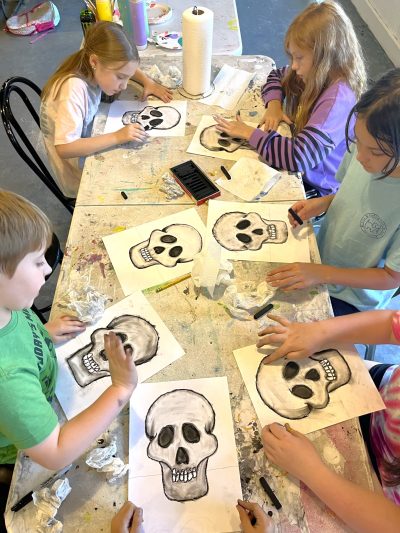 A group of kids drawing skulls at a table.