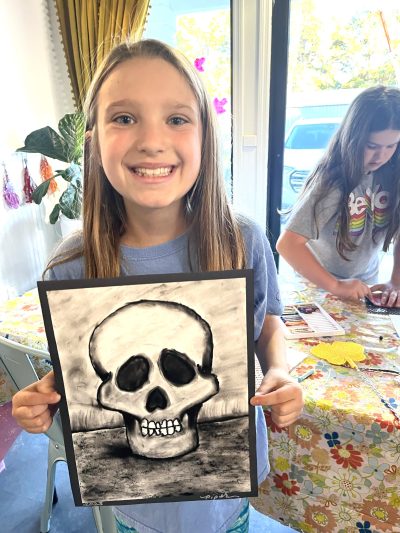 A girl holding up a drawing of a skull.