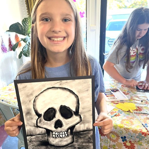 A girl holding up a drawing of a skull.