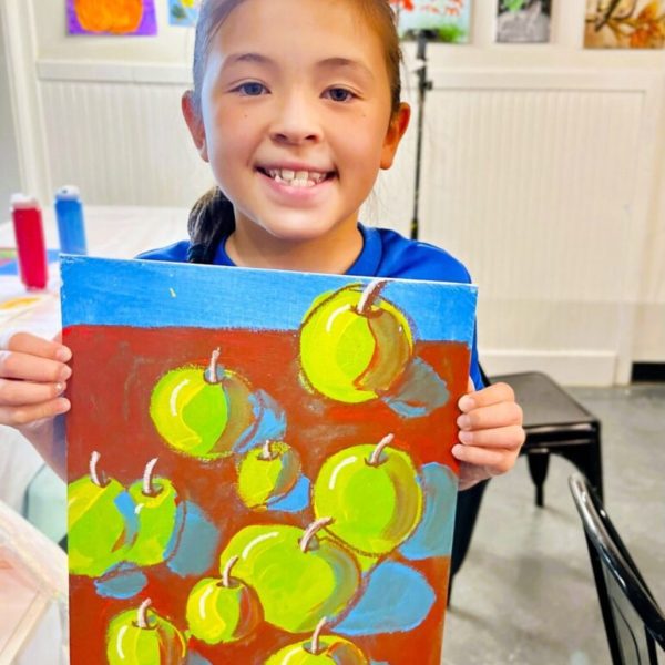 a girl is holding up a painting of apples
