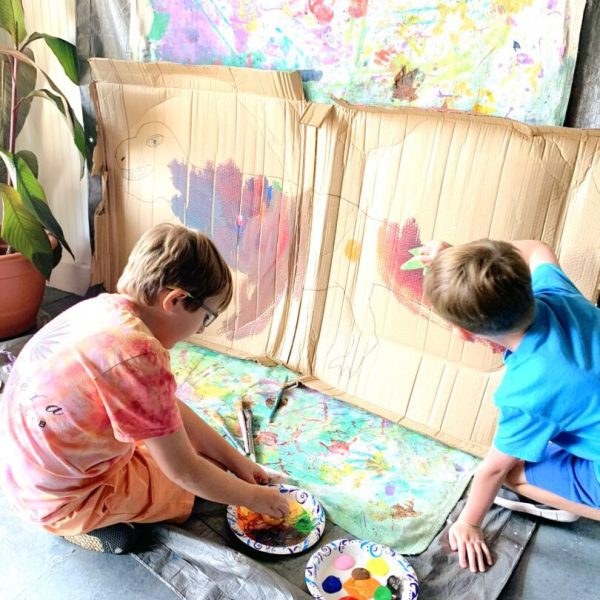 Two young boys painting with paint on a canvas.
