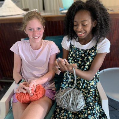 Two girls sitting on a chair and holding yarn.