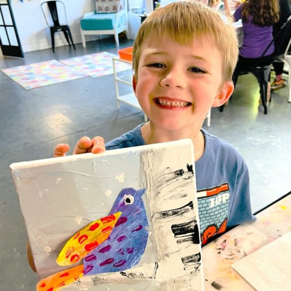 a boy is holding up a painting of a bird